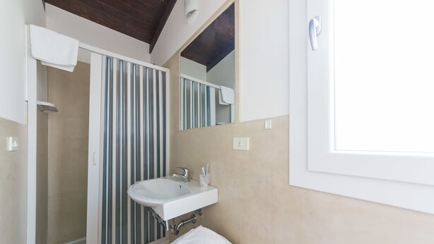 A bathroom with a white sink, a mirror, and a shower with vertical stripes. - Nicolaus Club Alimini Smile  (Otranto)