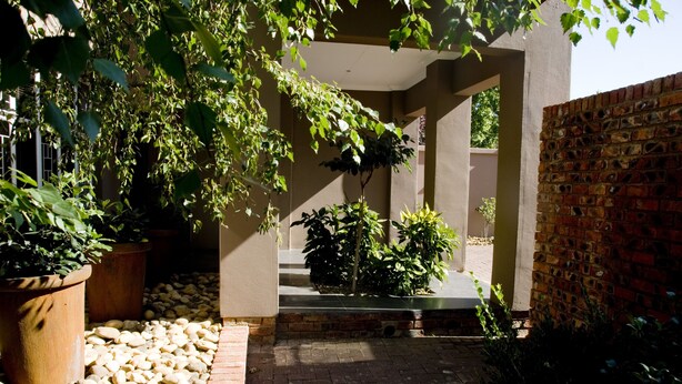 A garden with potted plants, a brick pathway, and a brick wall. - The Crown Guesthouse (Bethlehem)