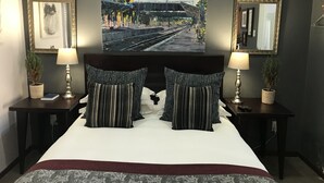 A bedroom with a large bed, two bedside tables with lamps, a painting above the bed, and two framed pictures on the walls. - The Crown Guesthouse (Bethlehem)