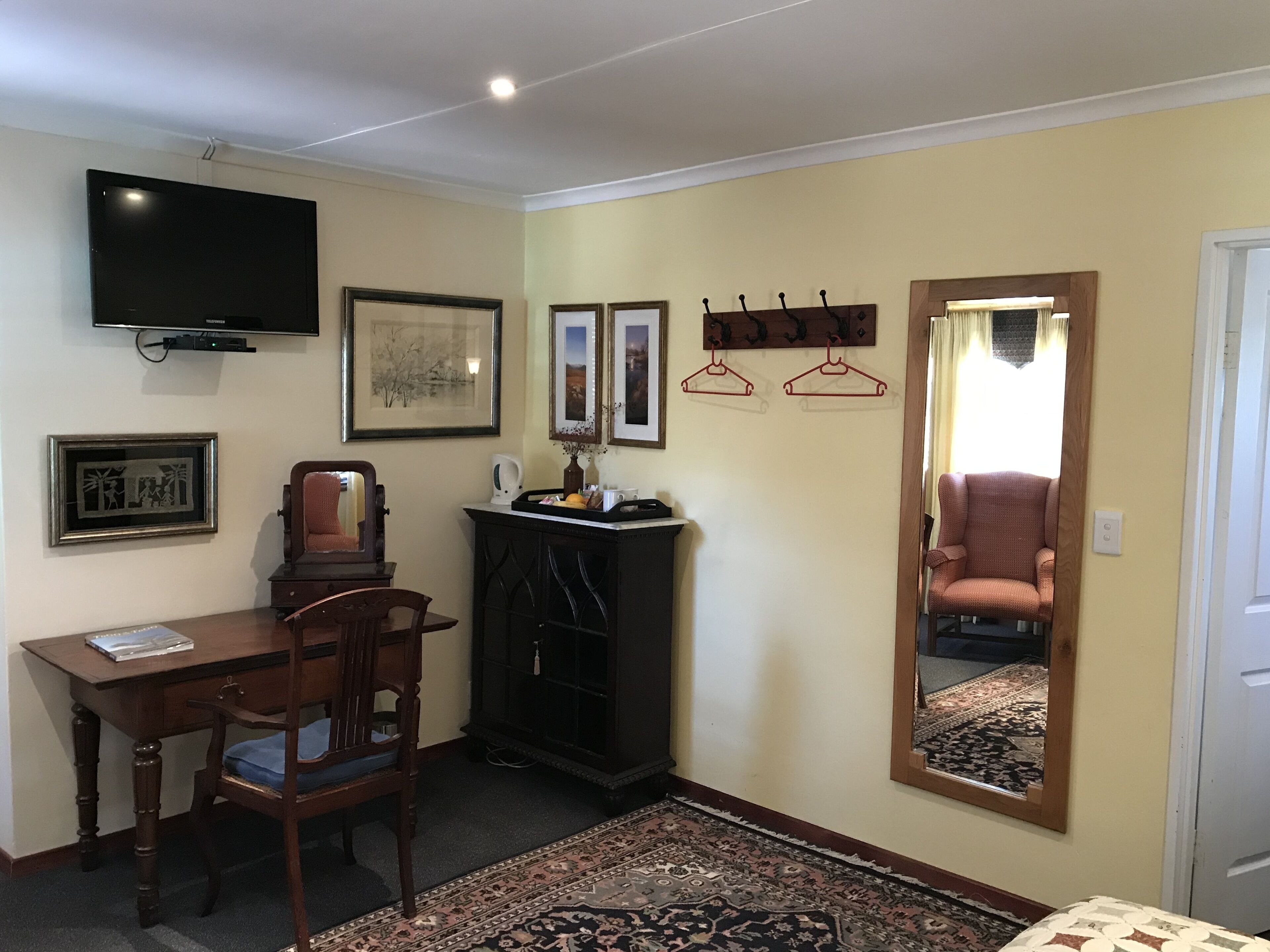 Una habitación con escritorio, silla, televisión, cuadro enmarco, ganchos para abrigos y un espejo que refleja una silla.