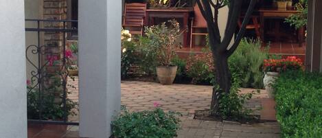 A courtyard with a brick pathway, potted plants, and a wooden table and chairs.
