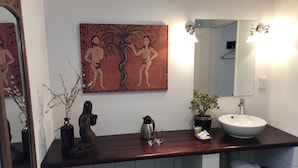 A bathroom with a wooden countertop, a white sink, a mirror, a painting, and a small potted plant. - The Crown Guesthouse (Bethlehem)