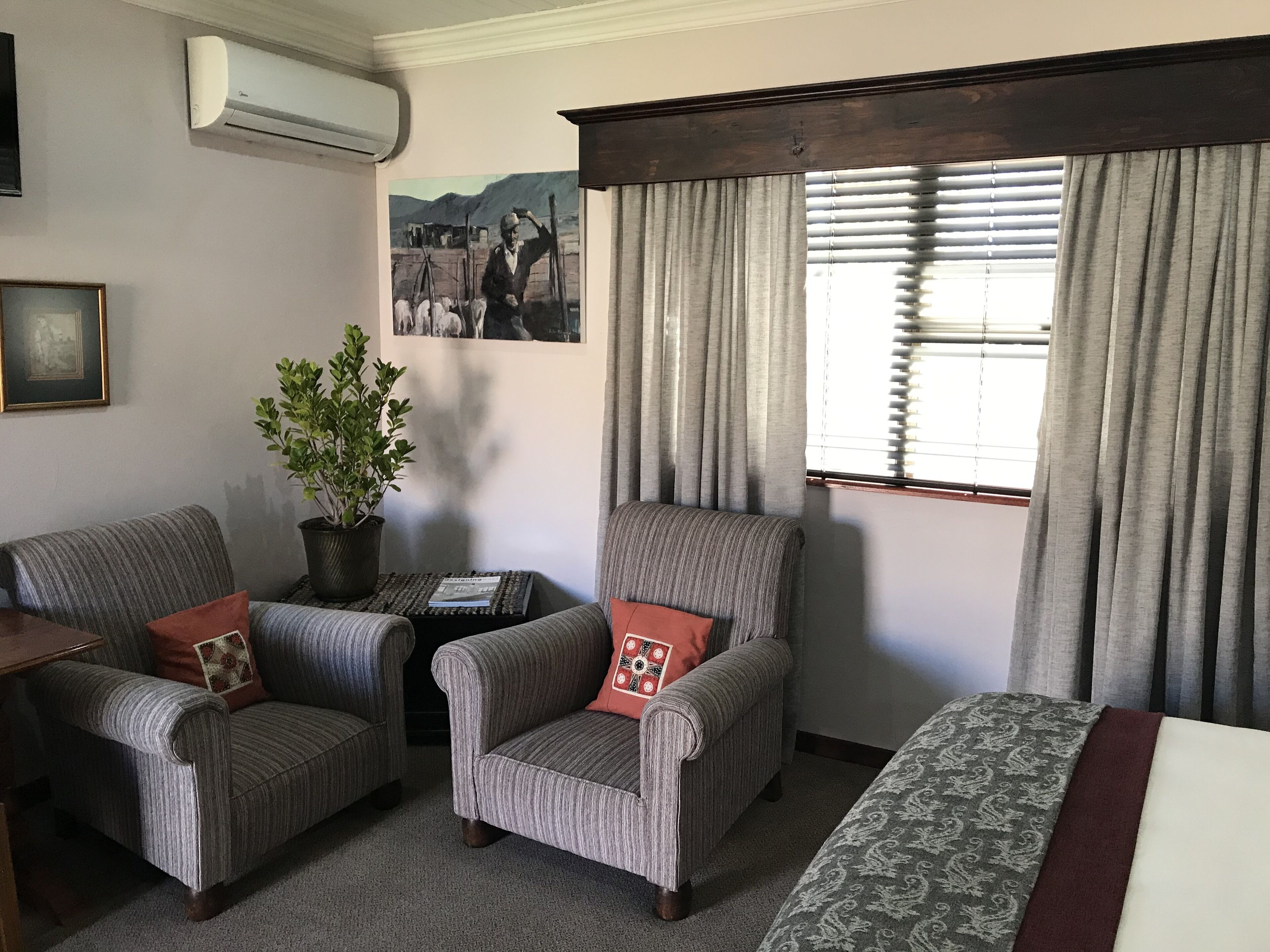 Una habitación con dos sillones, un sofá, una planta en maceta, un cuadro enmarco y una ventana con cortinas.