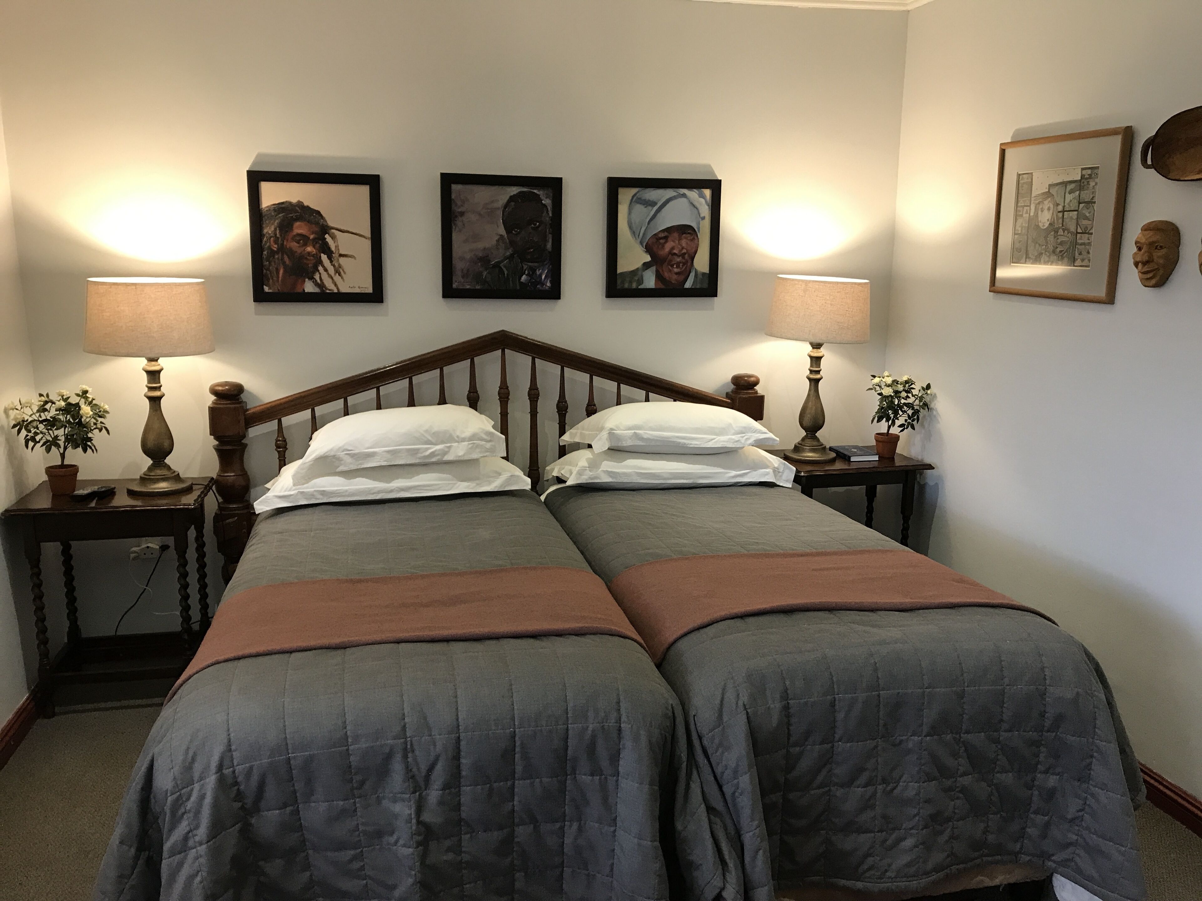 A double bed with two pillows, a wooden headboard, and two bedside tables with lamps and potted plants.