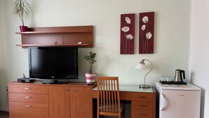 Habitación compacta con escritorio de madera, televisión, una silla, un refrigerador pequeño y una planta en maceta.