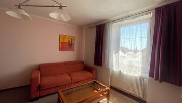 A living room with a red sofa, a glass-top coffee table, a ceiling fan, and a window with purple curtains.