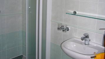 Un baño con cabina de ducha de vidrio, un lavamanos con espejo y una repisa de vidrio.