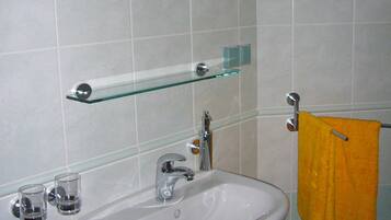 A bathroom with a white sink, two mirrors, a glass shelf, and a yellow towel.