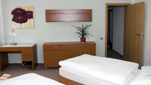 Un dormitorio con cama, escritorio, cómoda, planta en maceta y un cuadro en la pared.