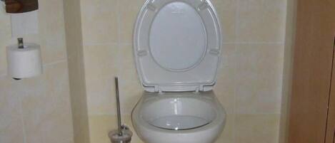 Un baño con inodoro, secador de manos y dispensador de toallas de papel.