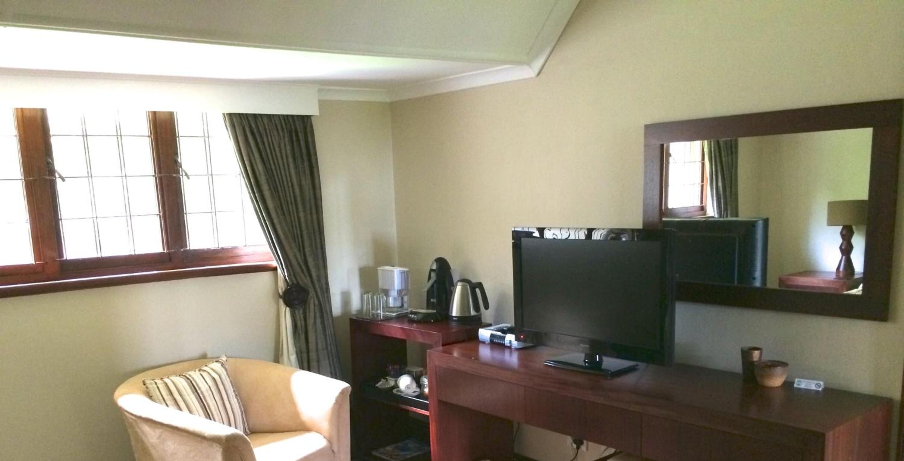 Habitación de hotel con escritorio, televisión, silla y ventana grande con cortinas.