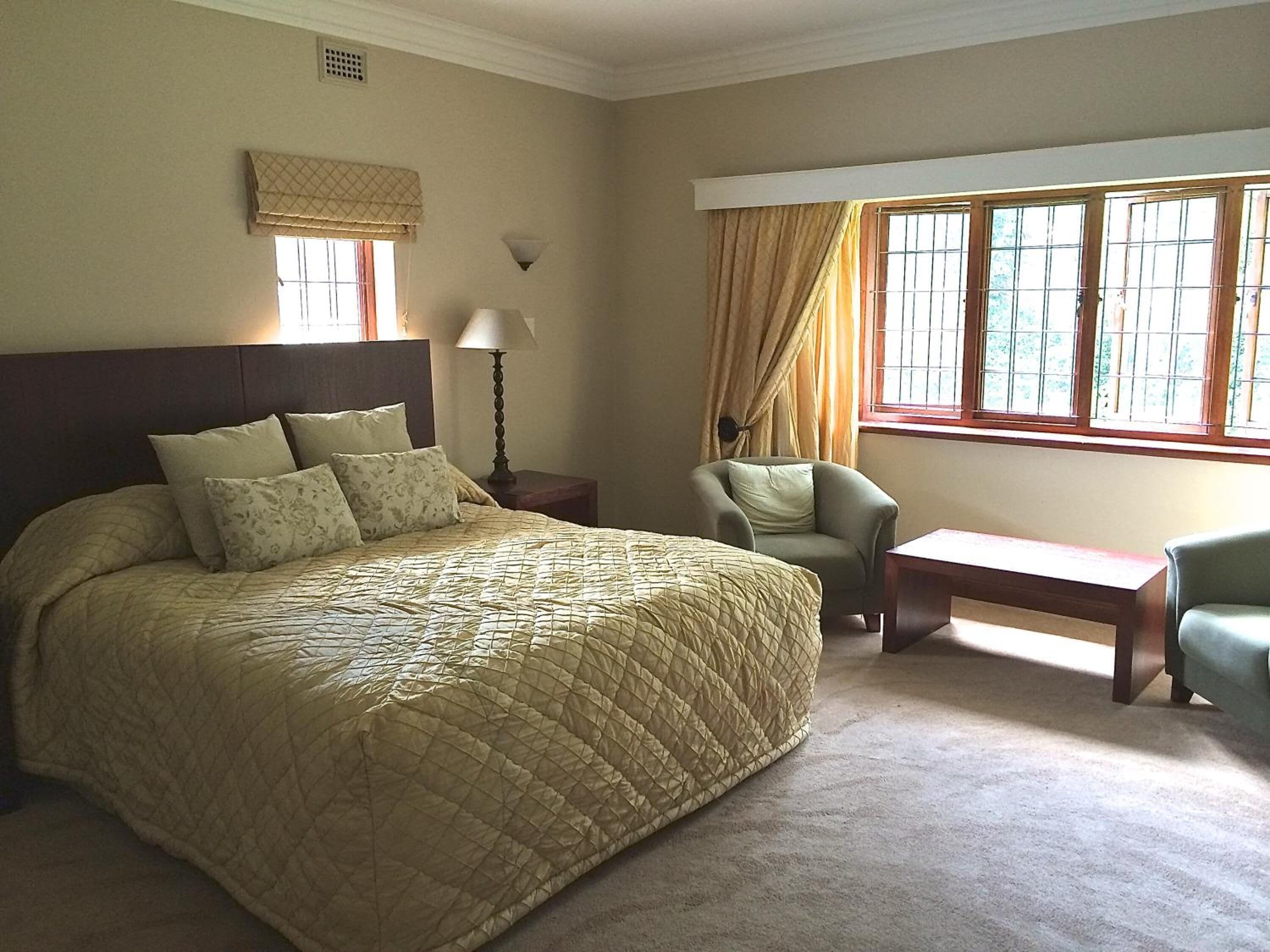A bedroom with a large bed, a chair, a nightstand, a lamp, and a window with curtains.