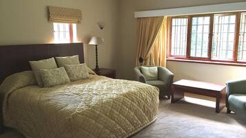 A bedroom with a large bed, a chair, a nightstand, a lamp, and a window with curtains.