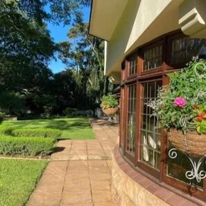 A house with a curved roof, large windows, and a well-maintained garden with a paved walkway. - Eagle Wind Manor (Botha's Hill)