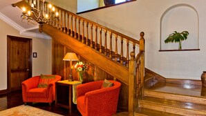 A grand staircase with wooden balusters, a chandelier, and a red armchair with a vase of flowers. - Eagle Wind Manor (Botha's Hill)