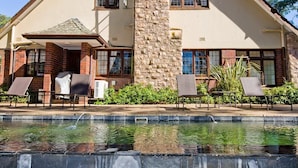 A two-story house with a stone chimney, a swimming pool, and outdoor seating. - Eagle Wind Manor (Botha's Hill)