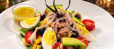 A plate of salad with various ingredients and a small bowl of dressing.
