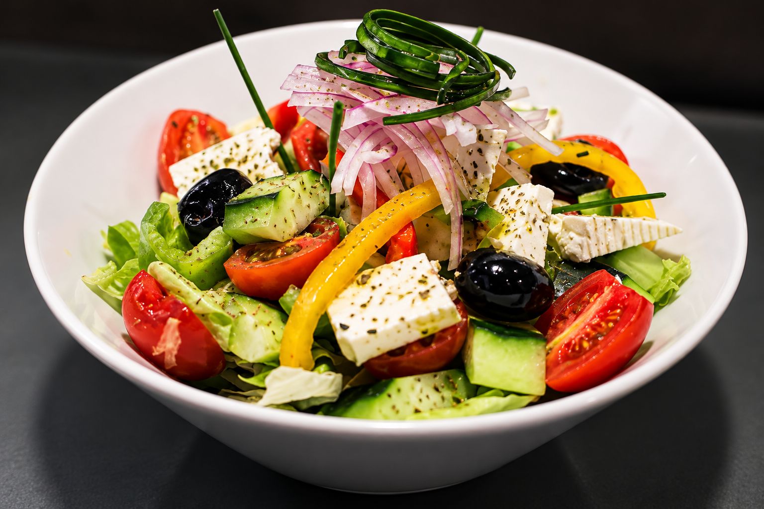 A white bowl containing a salad with various vegetables and feta cheese.