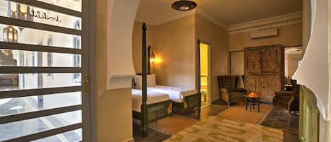 Habitación de hotel con cama, una zona de estar con sillón y mesa, una alfombra decorativa y vistas a través de un ventanal.