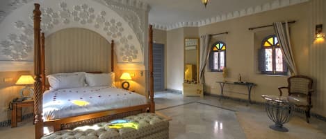 A spacious bedroom with a four-poster bed, a sitting area with a table and chairs, and a decorative mirror.