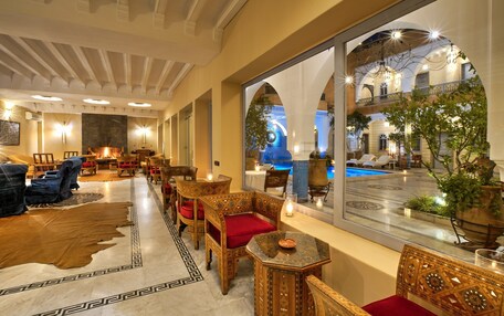 A hotel lobby with ornate wooden furniture, a large mirror reflecting the pool area, and a cozy seating arrangement.