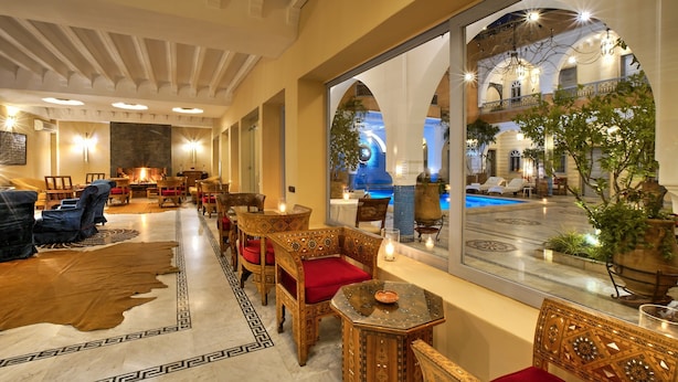 Vestíbulo de hotel con muebles de madera ornamentados, un espejo grande que refleja la zona de la piscina y una acogedora zona de estar.