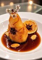 Un postre en un plato blanco con salsa, adornado con flores y anís estrellado.