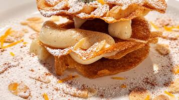 Un postre con capas, adornado con hojas de menta y ralladura de naranja, espolvoreado con azúcar glas y canela.