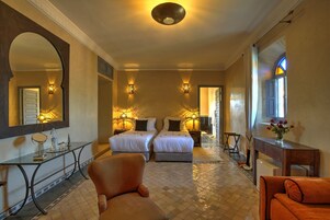 Una camera d'albergo con due letti, un angolo salotto con una poltrona, un comò con specchio e un tavolino.