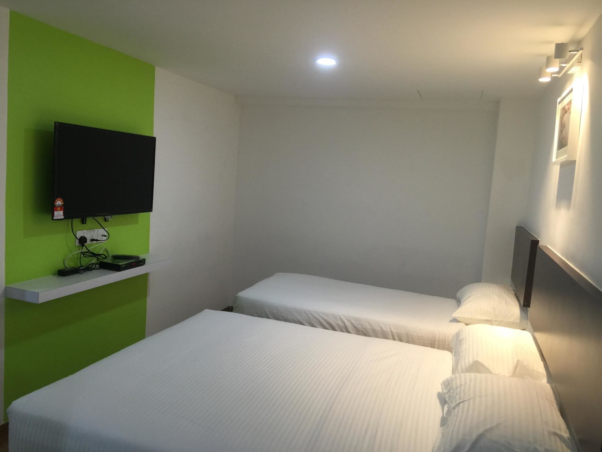 Hotelkamer met twee eenpersoonsbedden, een flatscreen televisie aan een groene muur en een klein plankje met een stekkerdoos.