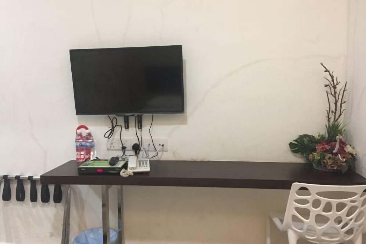 Een kamer met een donker bureau, een wandgemonteerde flatscreen-tv, een kleine plant in pot en een witte stoel.