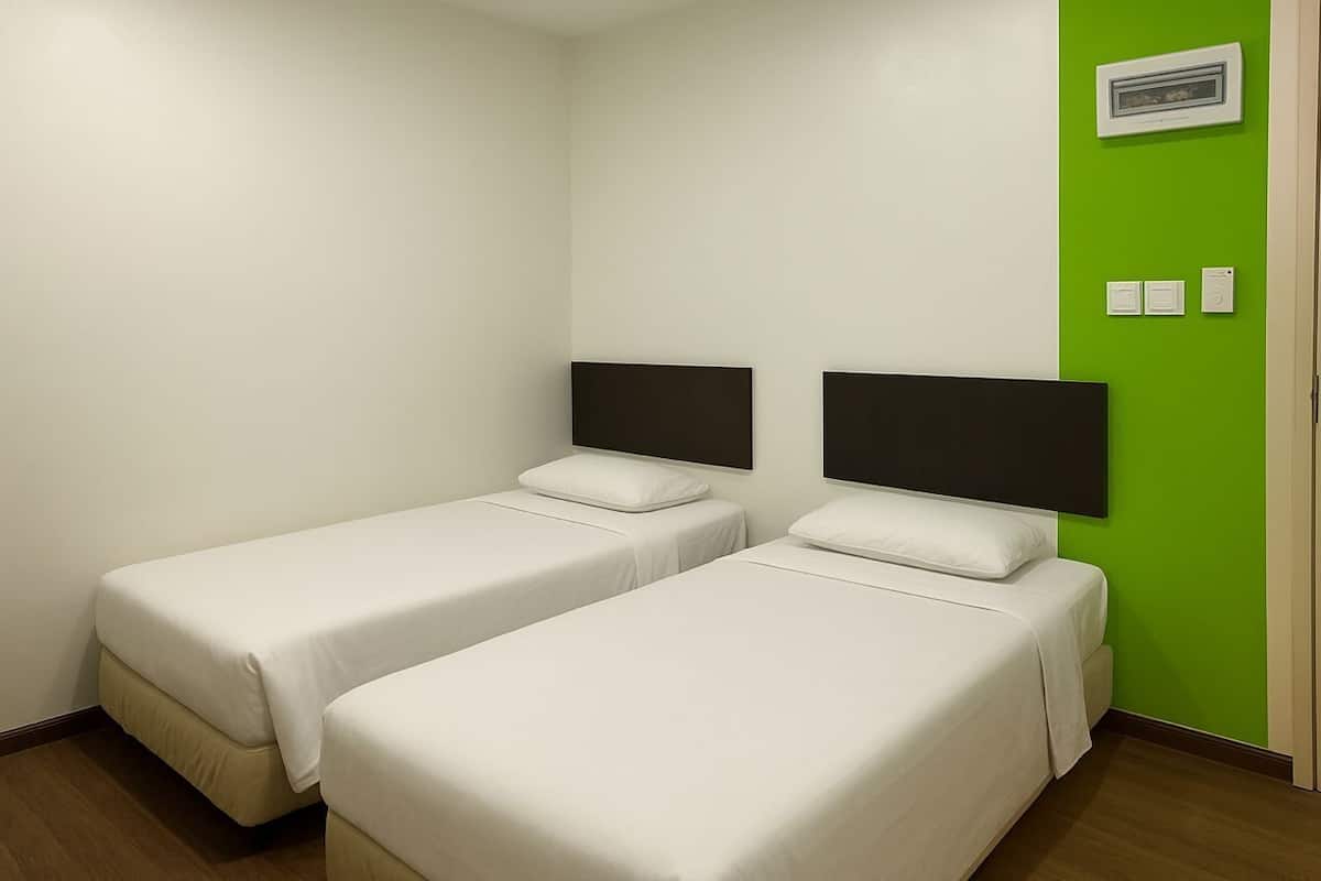 A room with two single beds, white bedding, a green accent wall, and a thermostat on the wall.
