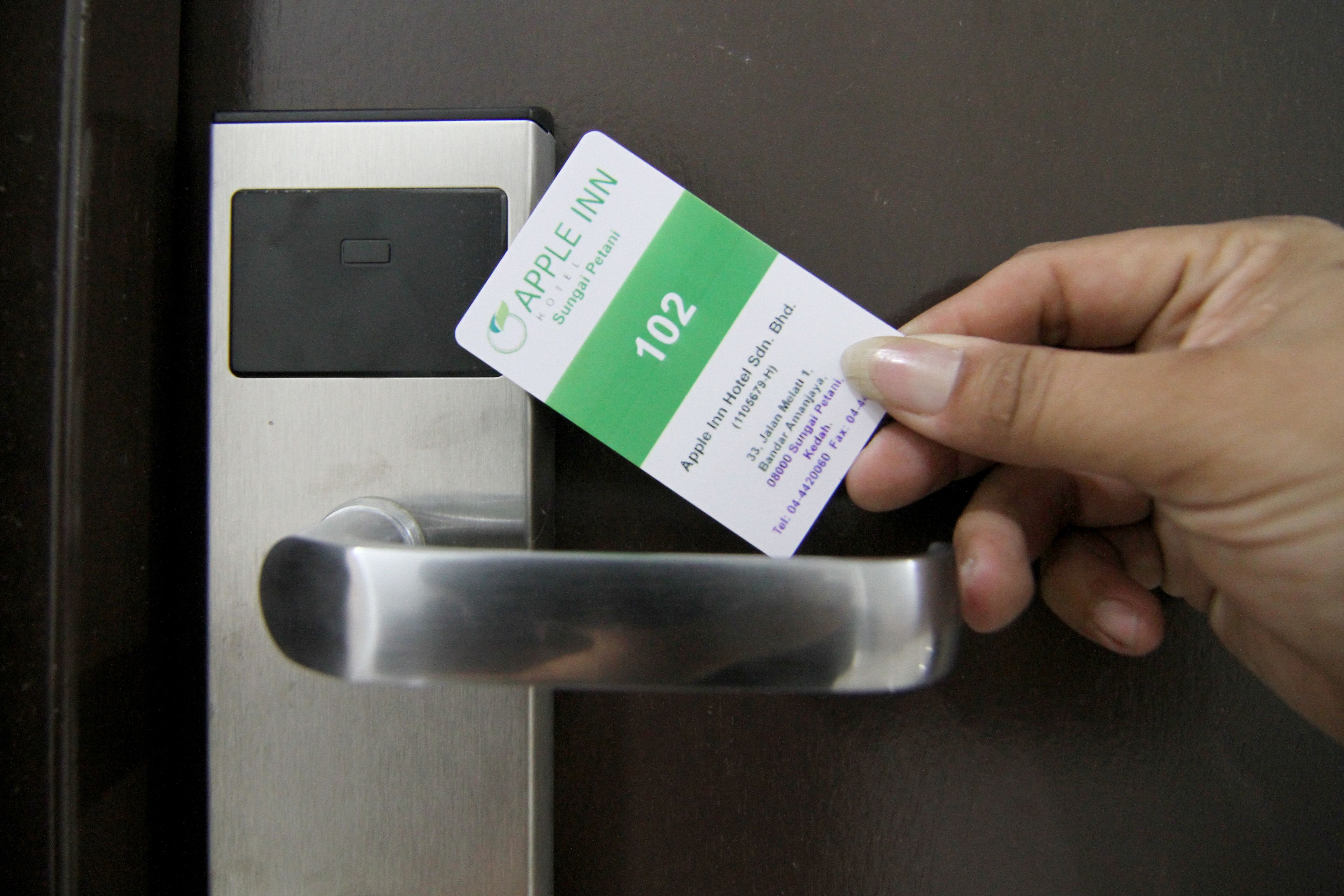 Une main tenant une carte sur laquelle est écrit « APPLE INN » et le numéro « 102 », devant une porte dotée d’un lecteur de carte magnétique.