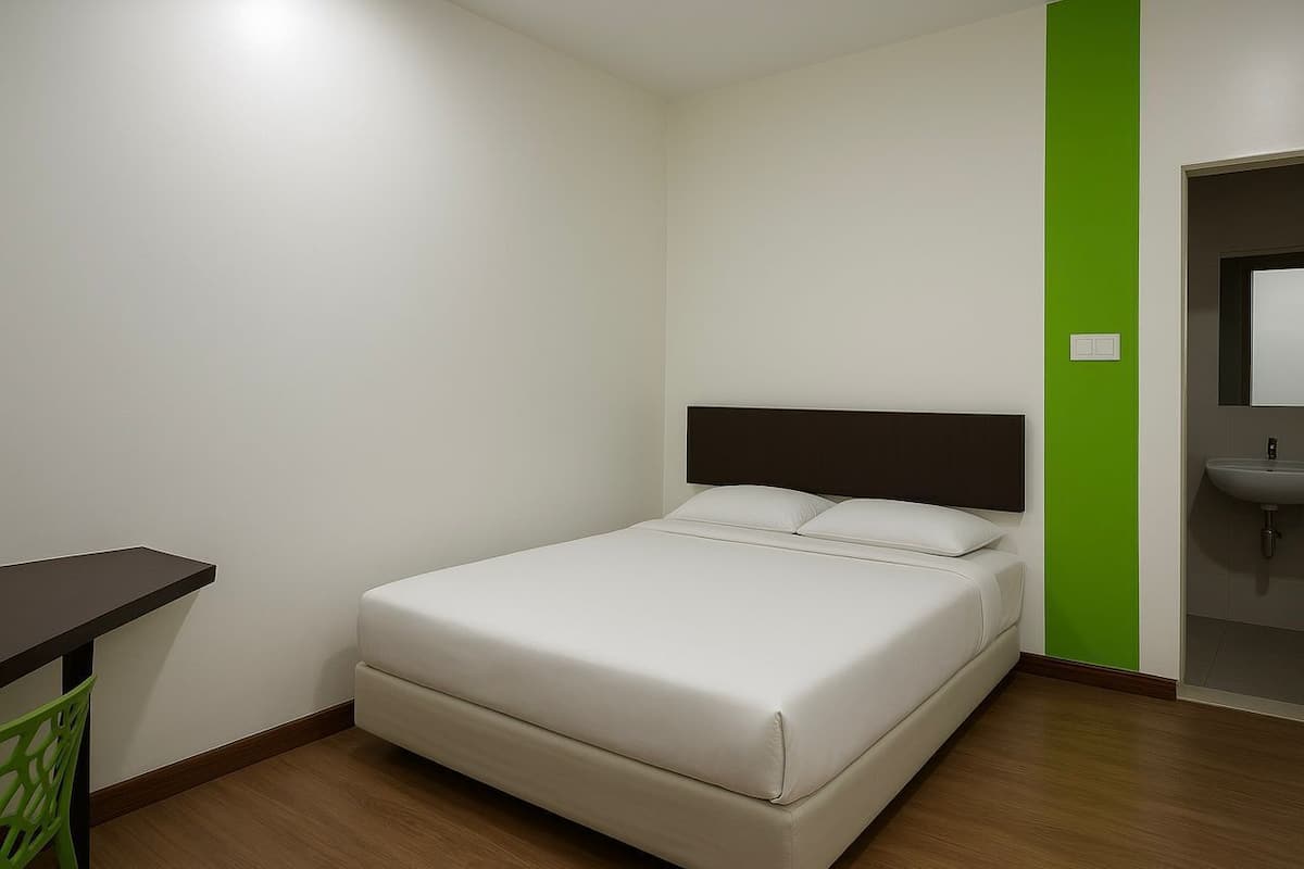 A small, neatly arranged room with a bed, a desk, and a green accent wall.
