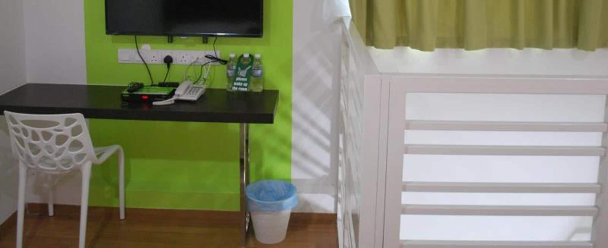 Une pièce comprenant un bureau, une chaise, un téléviseur fixé au mur et une fenêtre avec des rideaux.