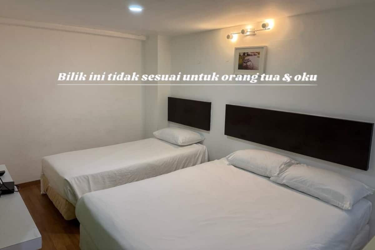 A hotel room with two single beds, a small desk, and a wall-mounted light fixture.