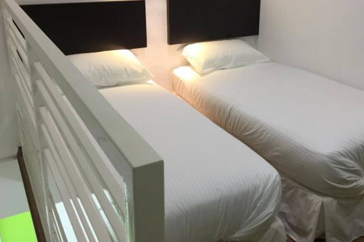 A single bed with white bedding in a room with white walls and a white railing.