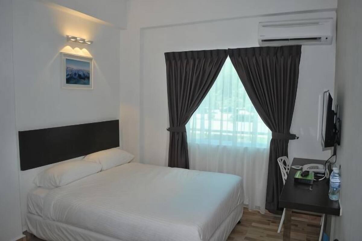 A hotel room with a bed, a desk with a chair, a television, and a window with curtains.