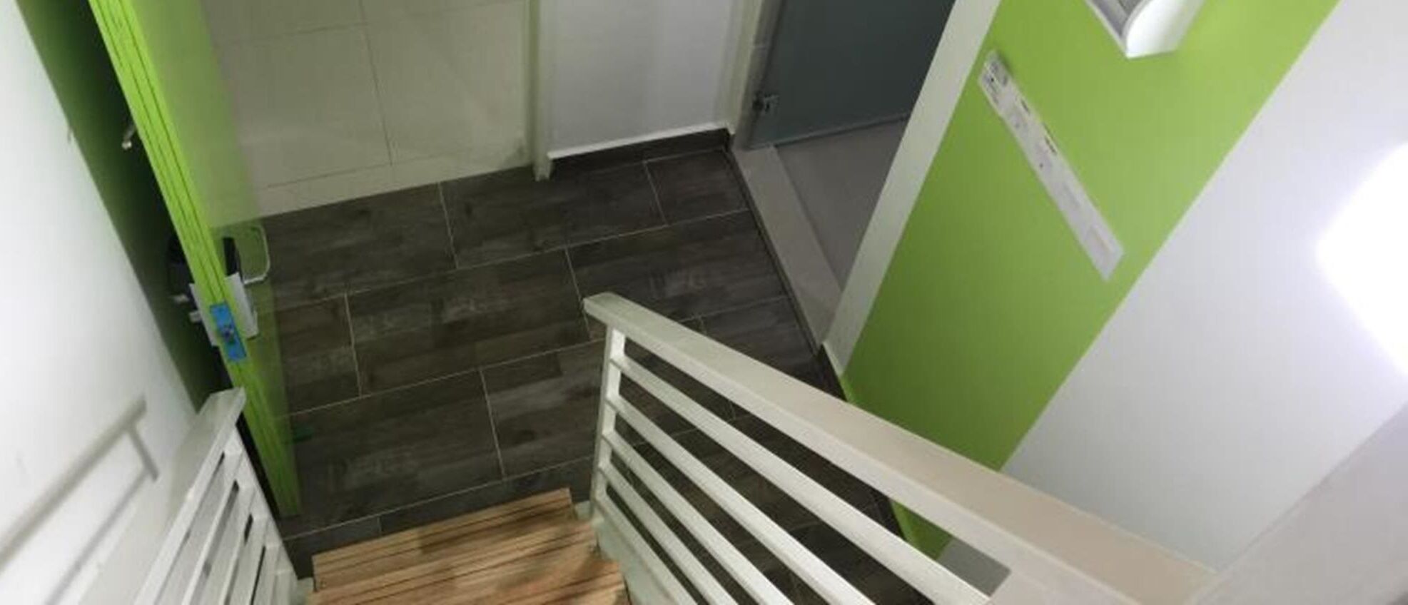 Una escalera con barandilla blanca, pared verde y suelo de baldosas.
