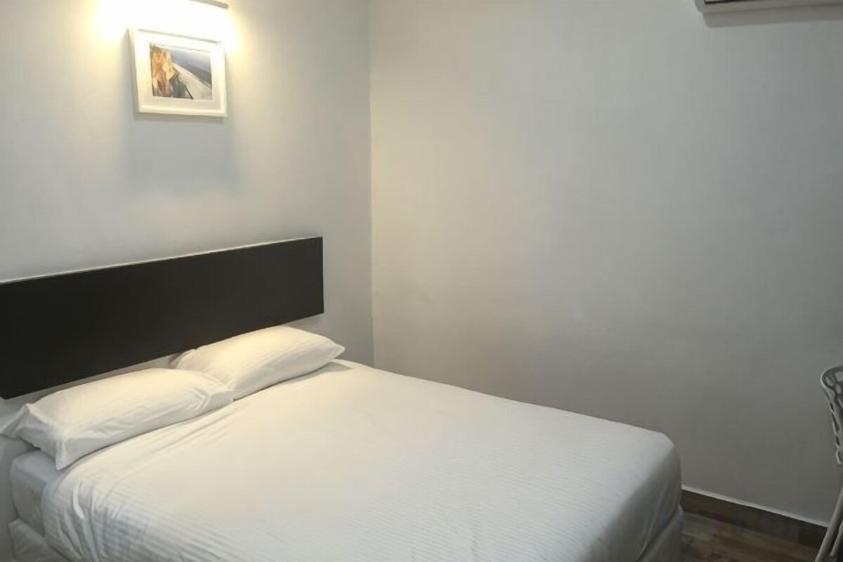 Een bed met een zwart hoofdeinde, witte beddengoed en een wandlamp.