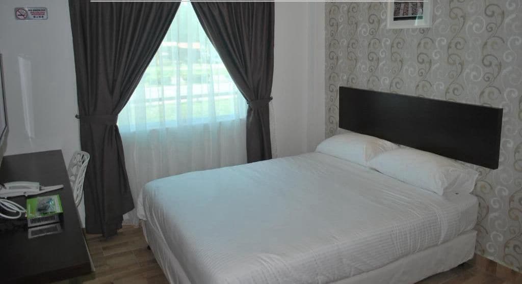 A hotel room with a bed, a desk with a phone and a small table, and a window with curtains.