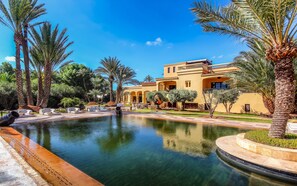 Un resort lujoso con piscina, palmeras y un edificio de estilo mediterráneo.