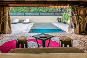 Una habitación con piscina, dos sillones blancos, una mesita y un tapete de estampado rojo.