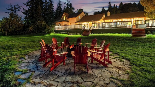 Eine Lodge mit einem Steinkamin und roten Adirondack-Stühlen davor.