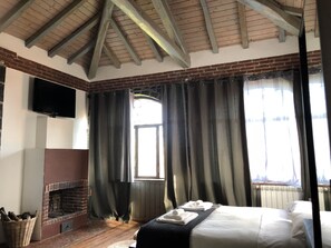 A room with a brick fireplace, a bed with white linens, and a television mounted on the wall. - B&B Villa Loriana (Milo)