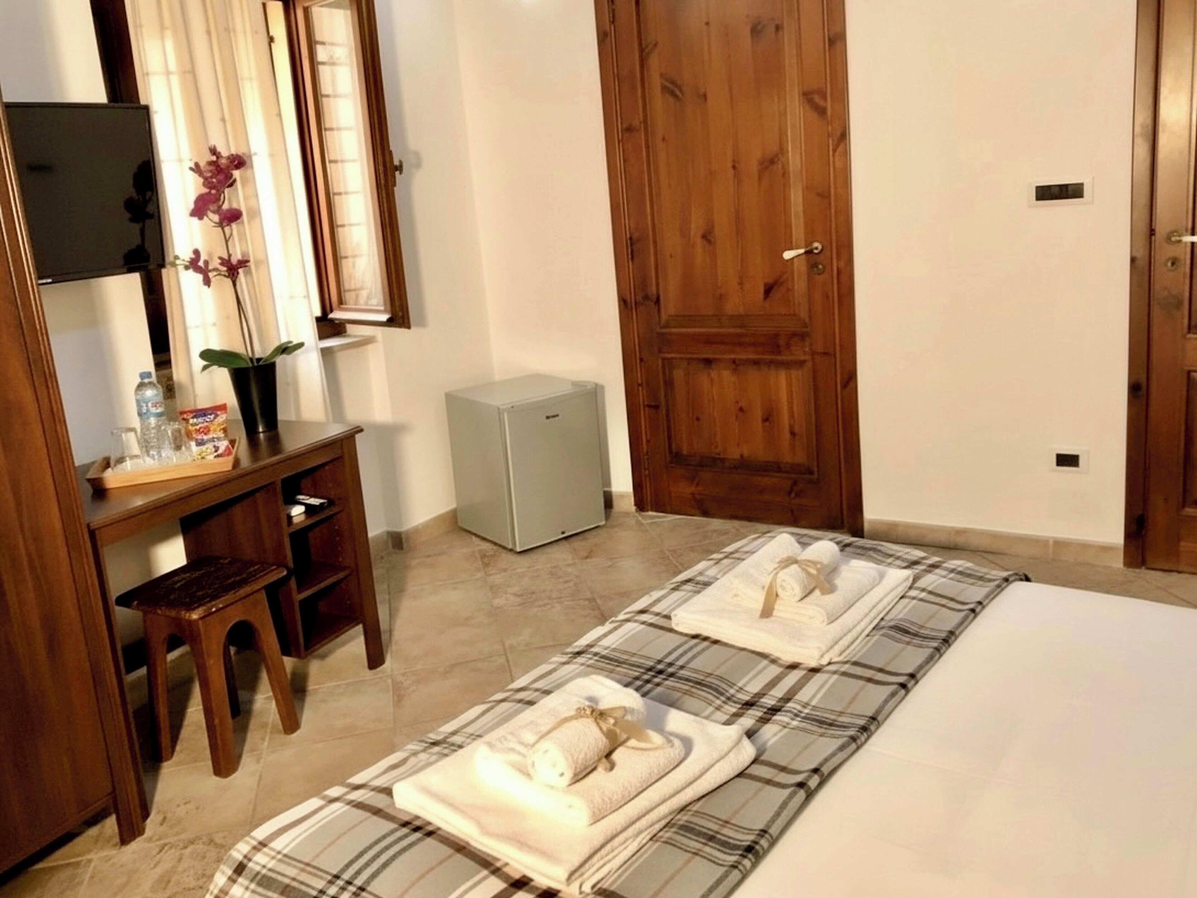 A hotel room with two beds, a small desk, a mirror, a wooden door, and a small refrigerator.