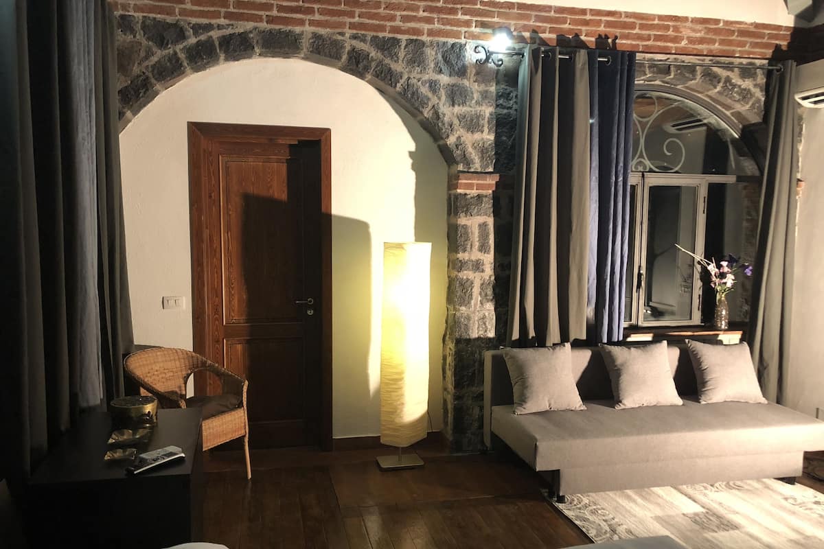 Une chambre avec une porte en bois, un canapé-lit, une chaise, une lampe et une fenêtre avec des rideaux.