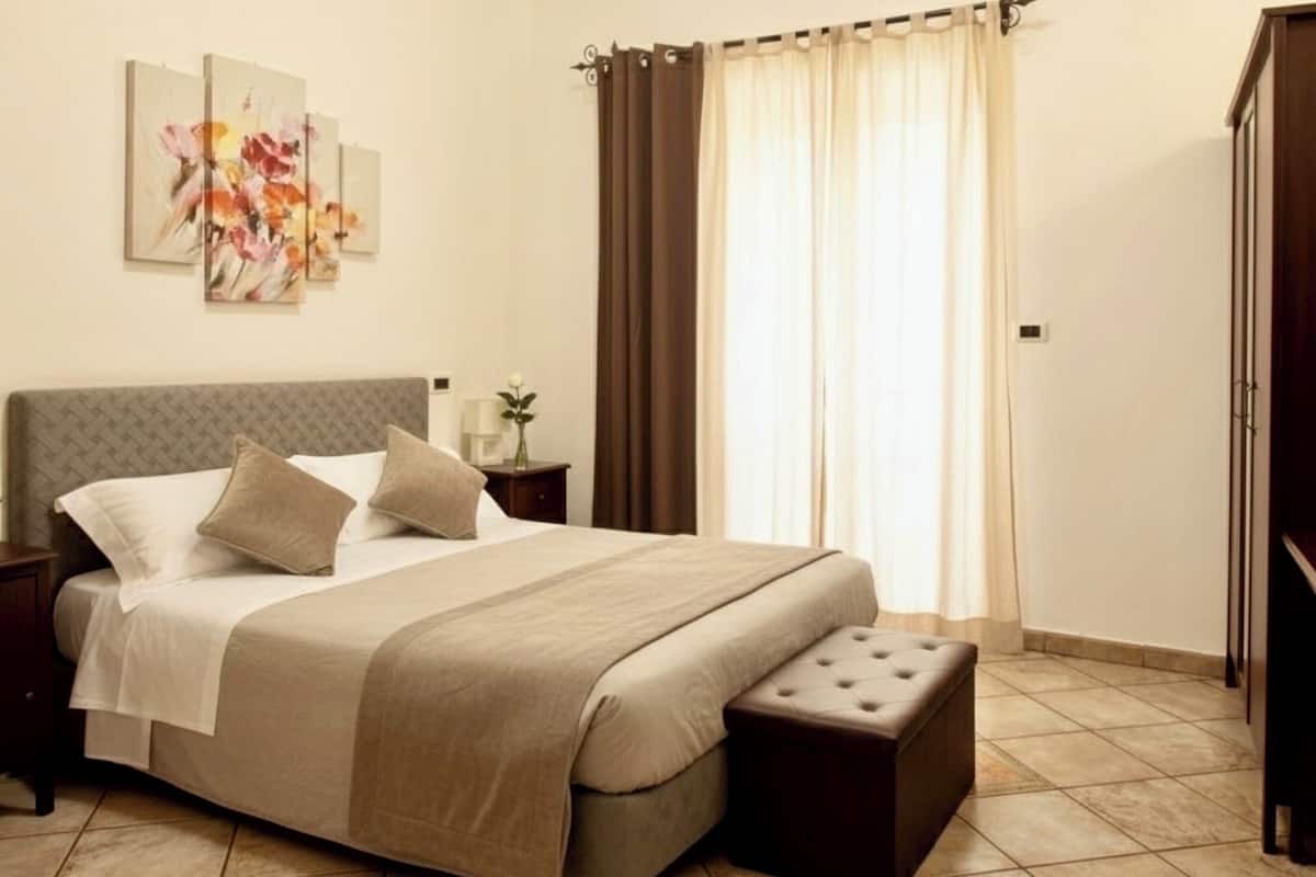 Une chambre à coucher bien rangée, avec un grand lit, une table de chevet, une commode et un coussin décoratif.
