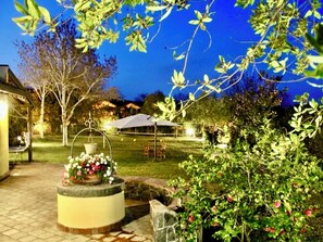 An outdoor patio area with a circular stone planter, a pergola, and a dining table under a canopy. - B&B Villa Loriana (Milo)