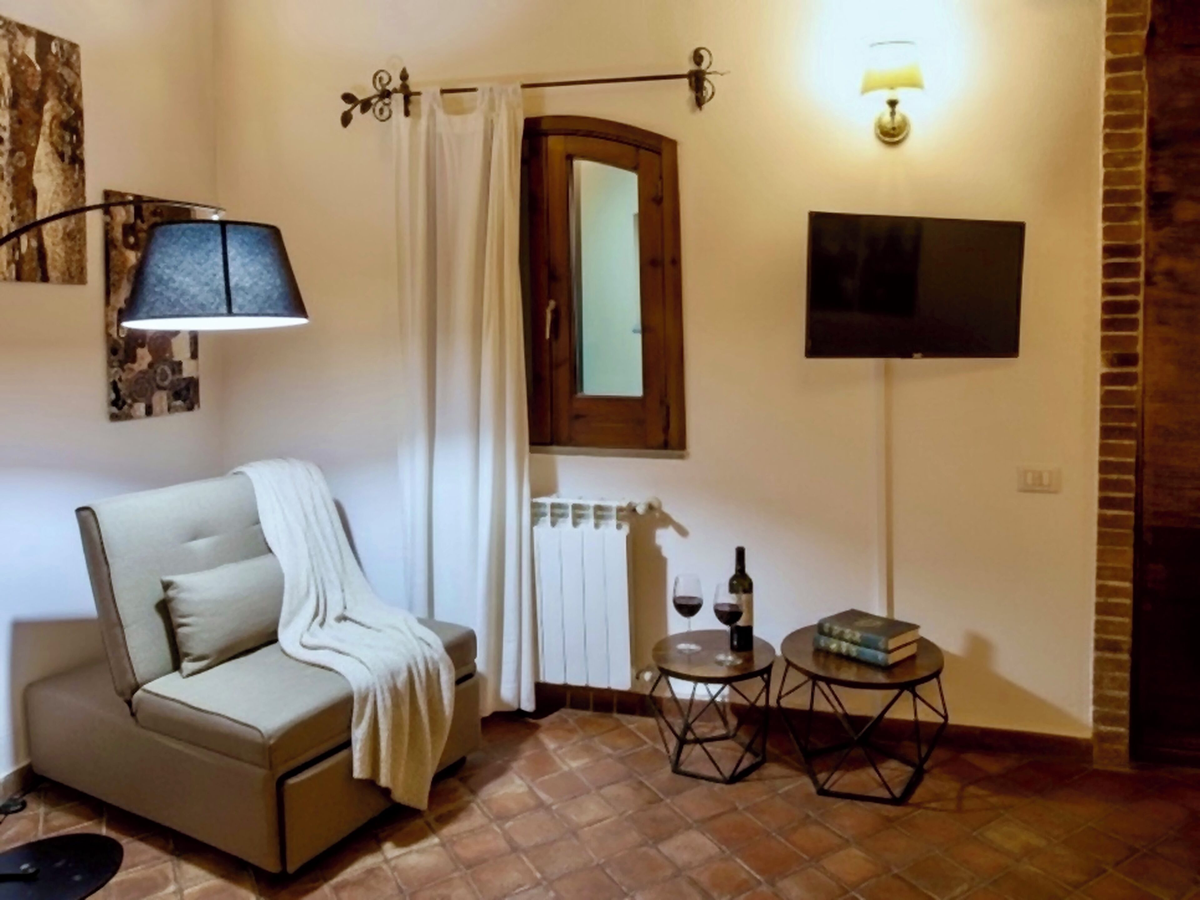 A cozy room with a sofa, a small table with a bottle and glasses, a TV, and a brick wall.